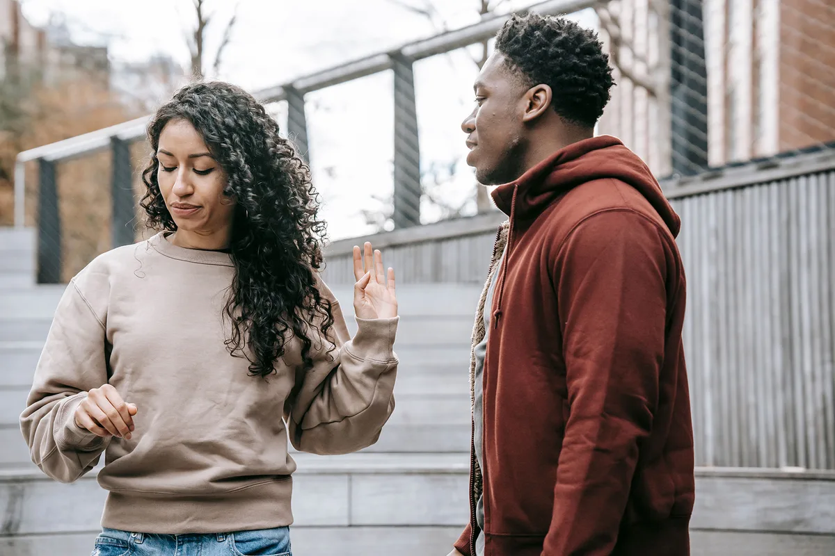 A couple arguing outdoors, one turning away with a raised hand as the other keeps talking