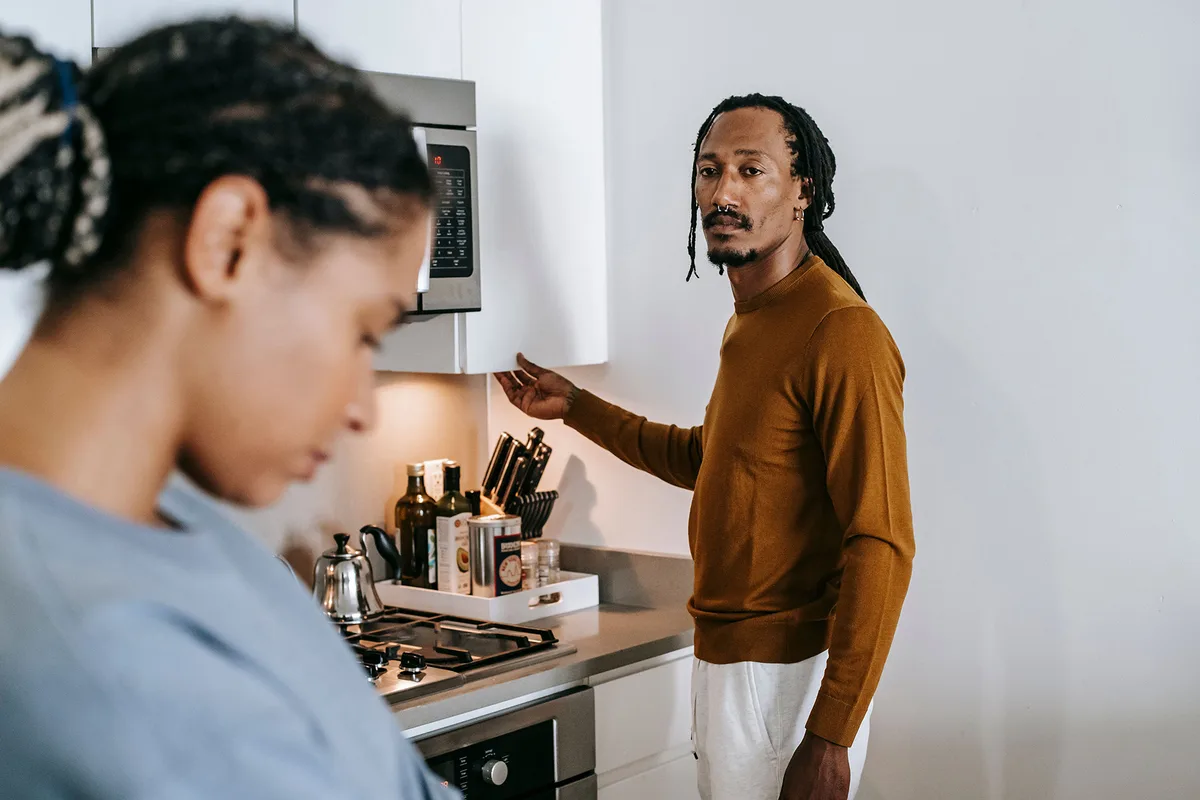 A man mid-sentence in a kitchen while his partner stands turned away, looking down