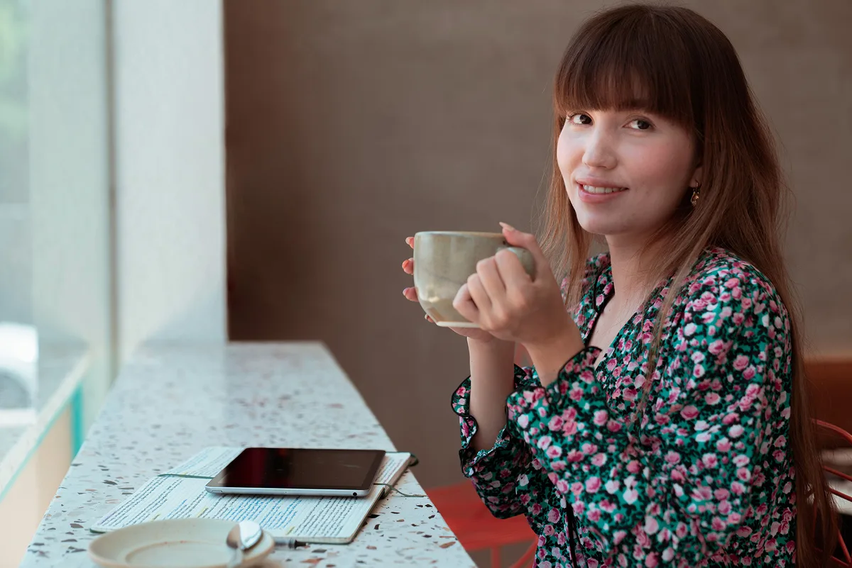 A woman sitting alone at a cafe counter with a coffee, looking off toward the window