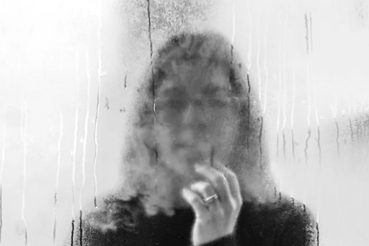 A figure blurred behind fogged glass, their features dissolving into the background